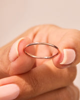 Delicate rose gold stacking ring held by a manicured hand