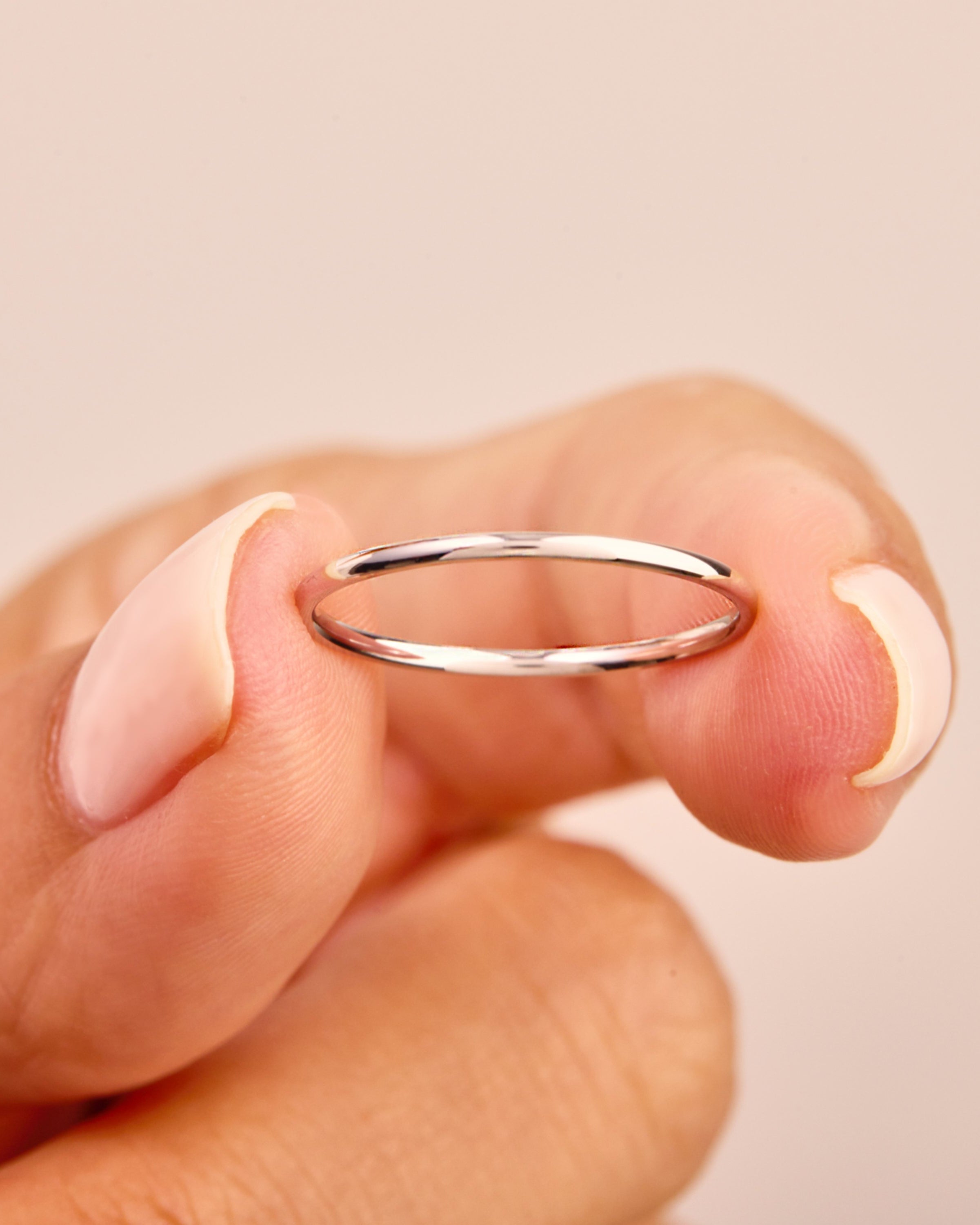Delicate silver band ring held by a manicured hand, jewelry