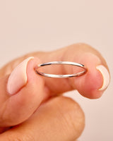 Delicate silver band ring held by a manicured hand, jewelry