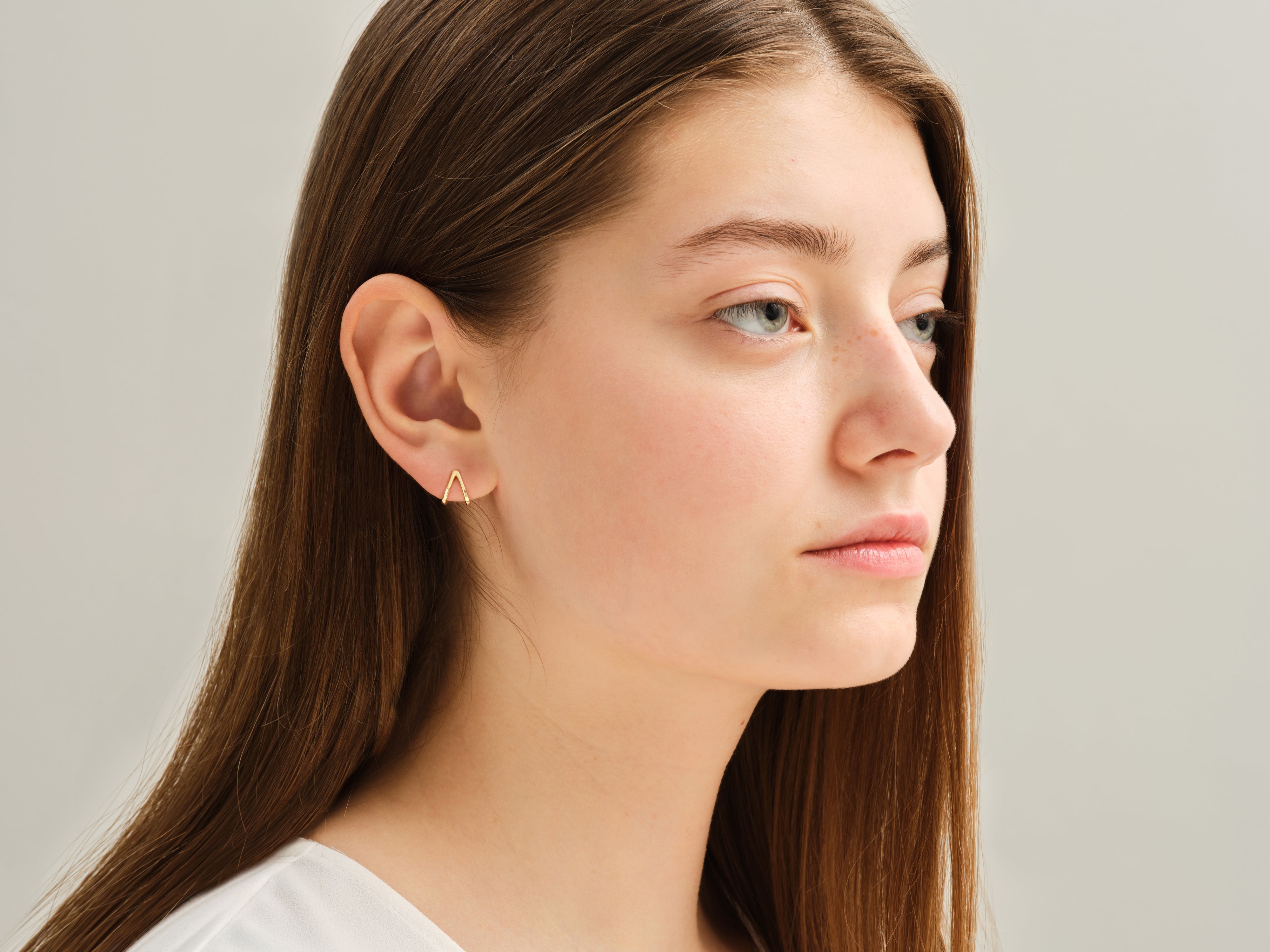 Gold triangle earrings on a woman's ear, jewelry product photography