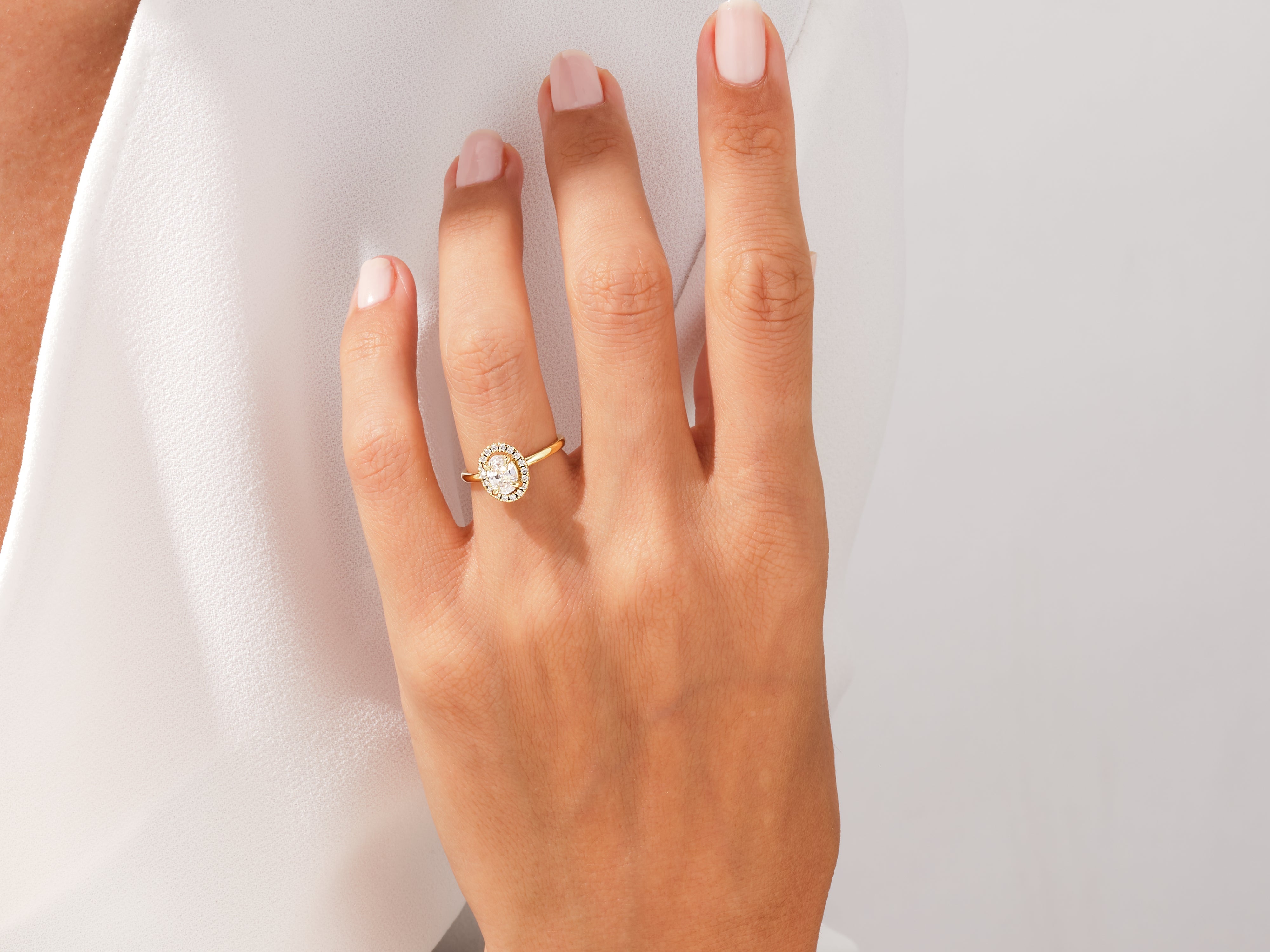 Gold oval halo diamond engagement ring on a woman's finger
