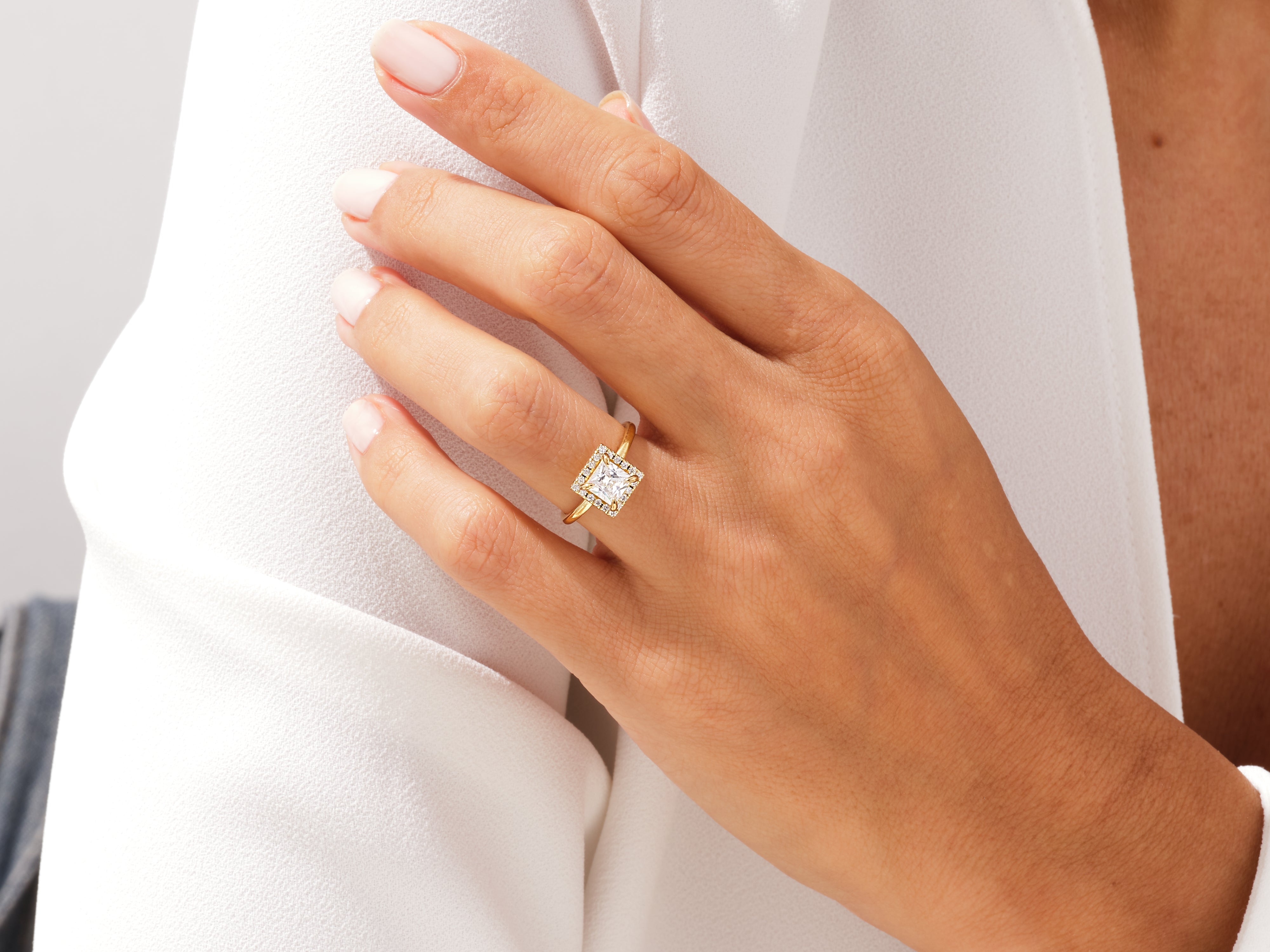 Gold diamond halo square engagement ring on hand