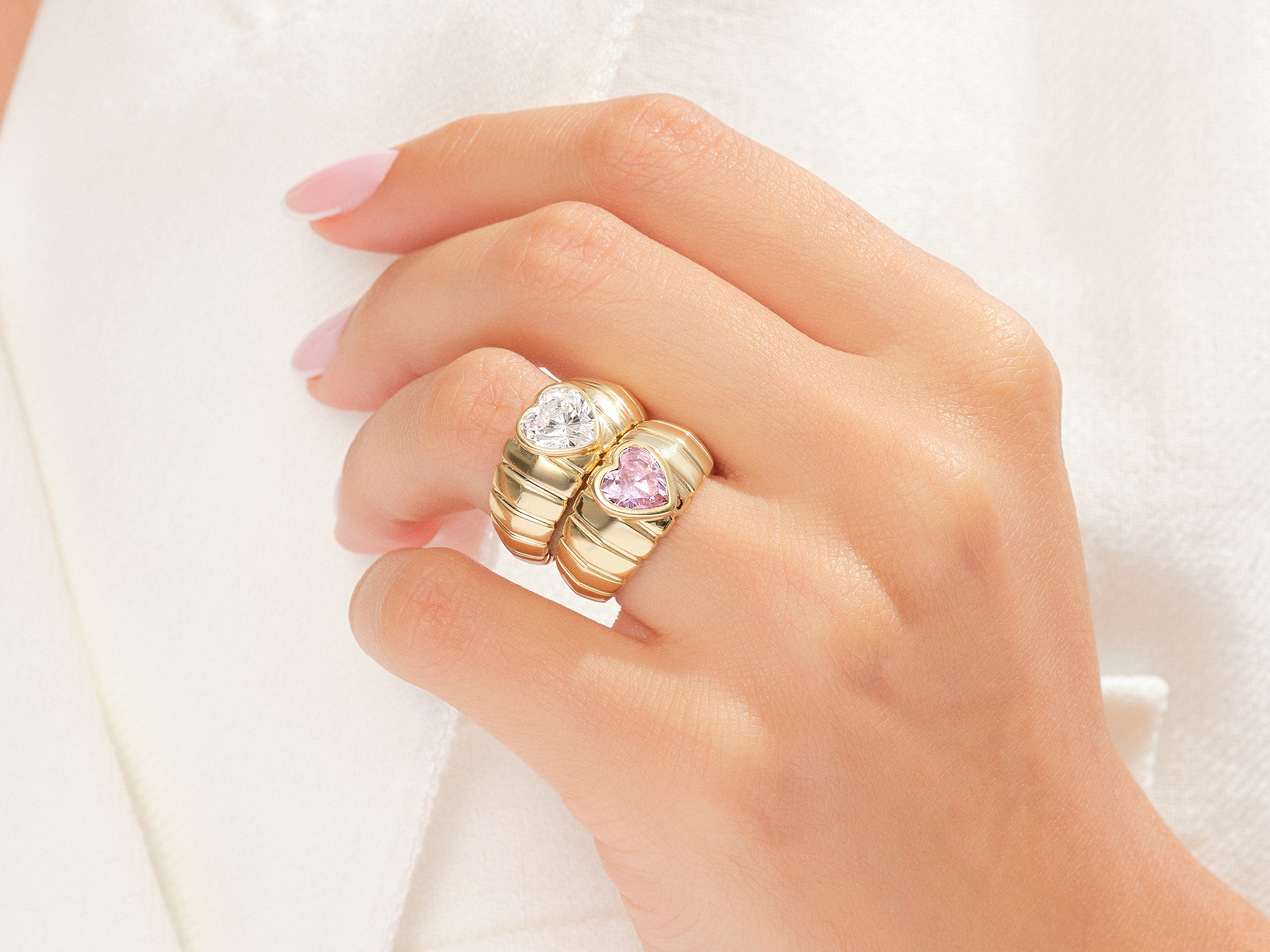 Gold heart rings with diamonds and pink stones on a hand