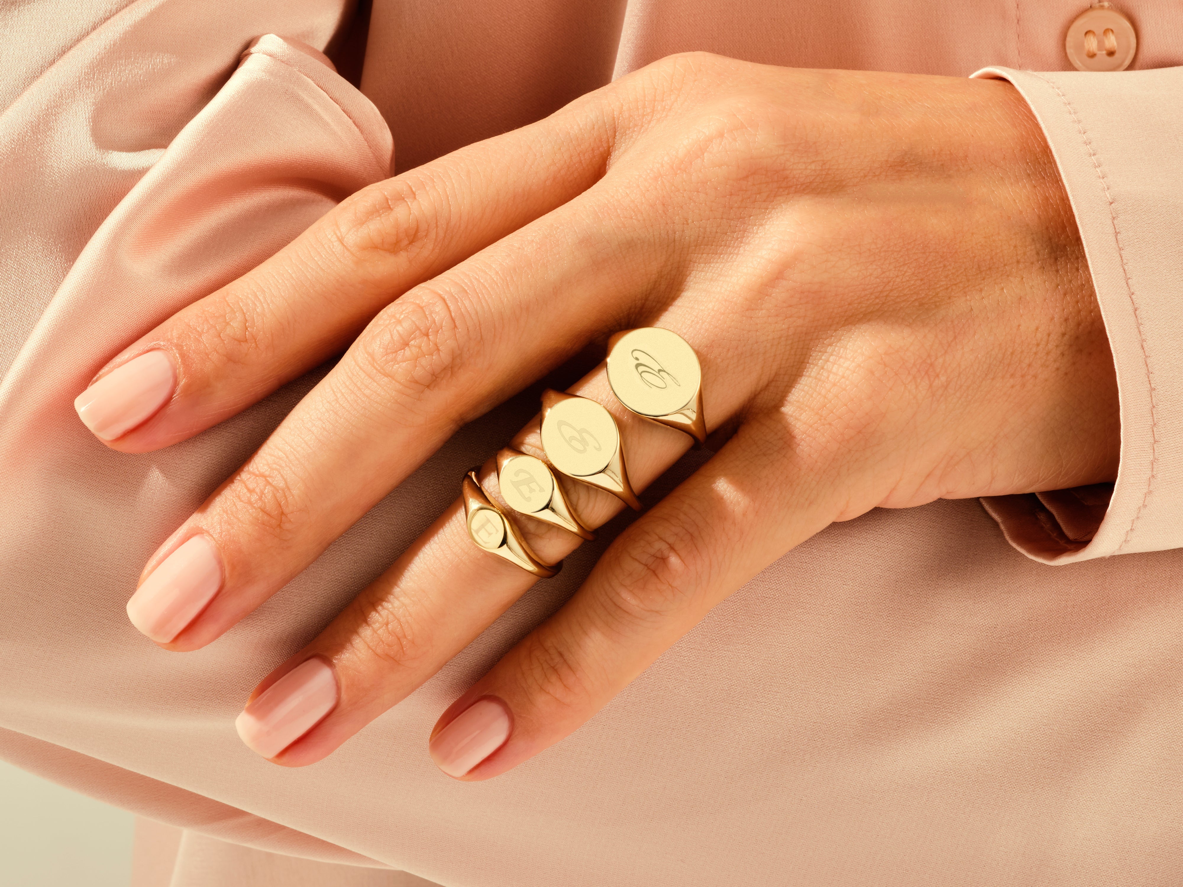 Gold signet rings with engraved initials on a hand