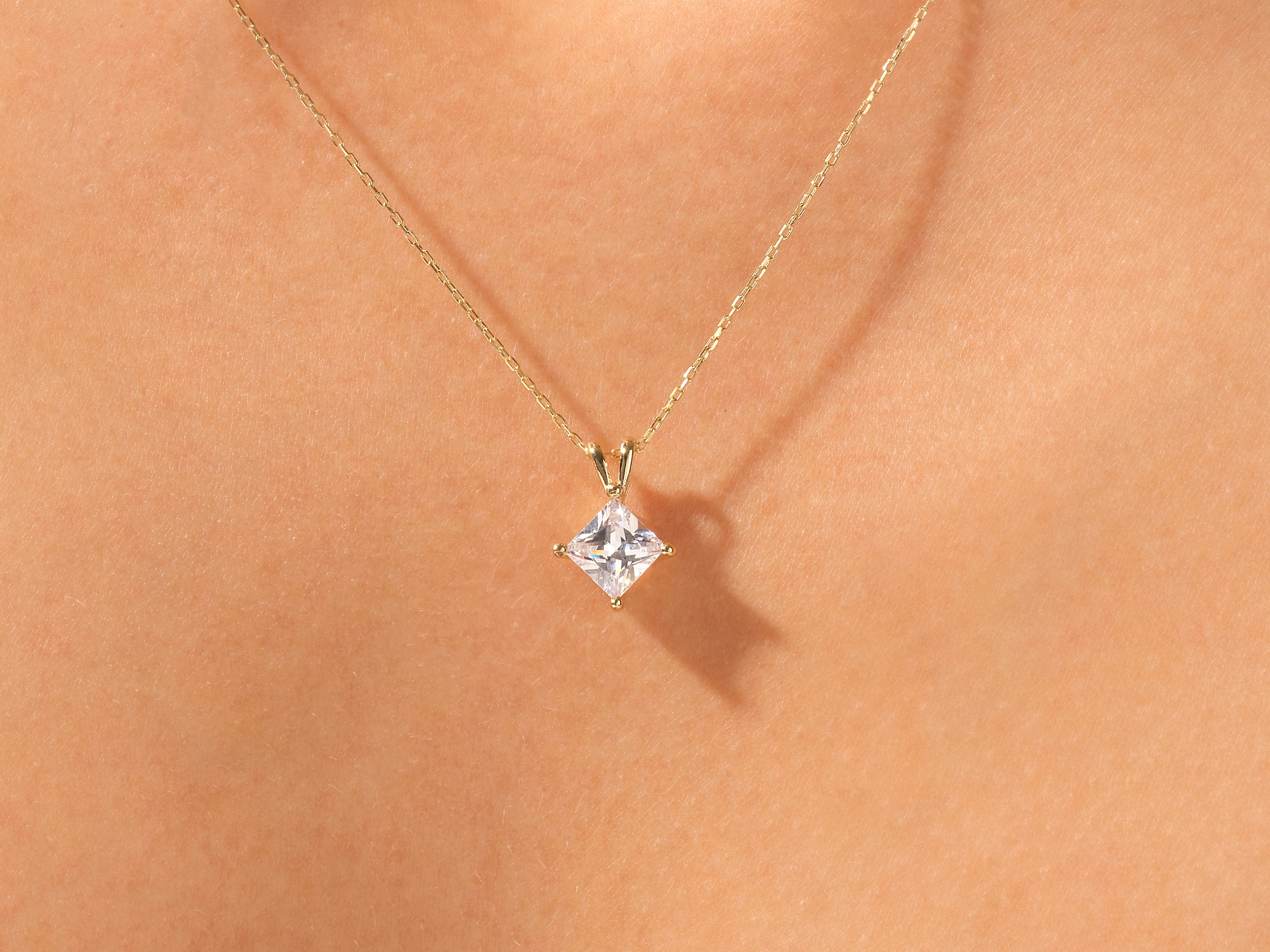 Gold necklace with princess cut diamond pendant on skin