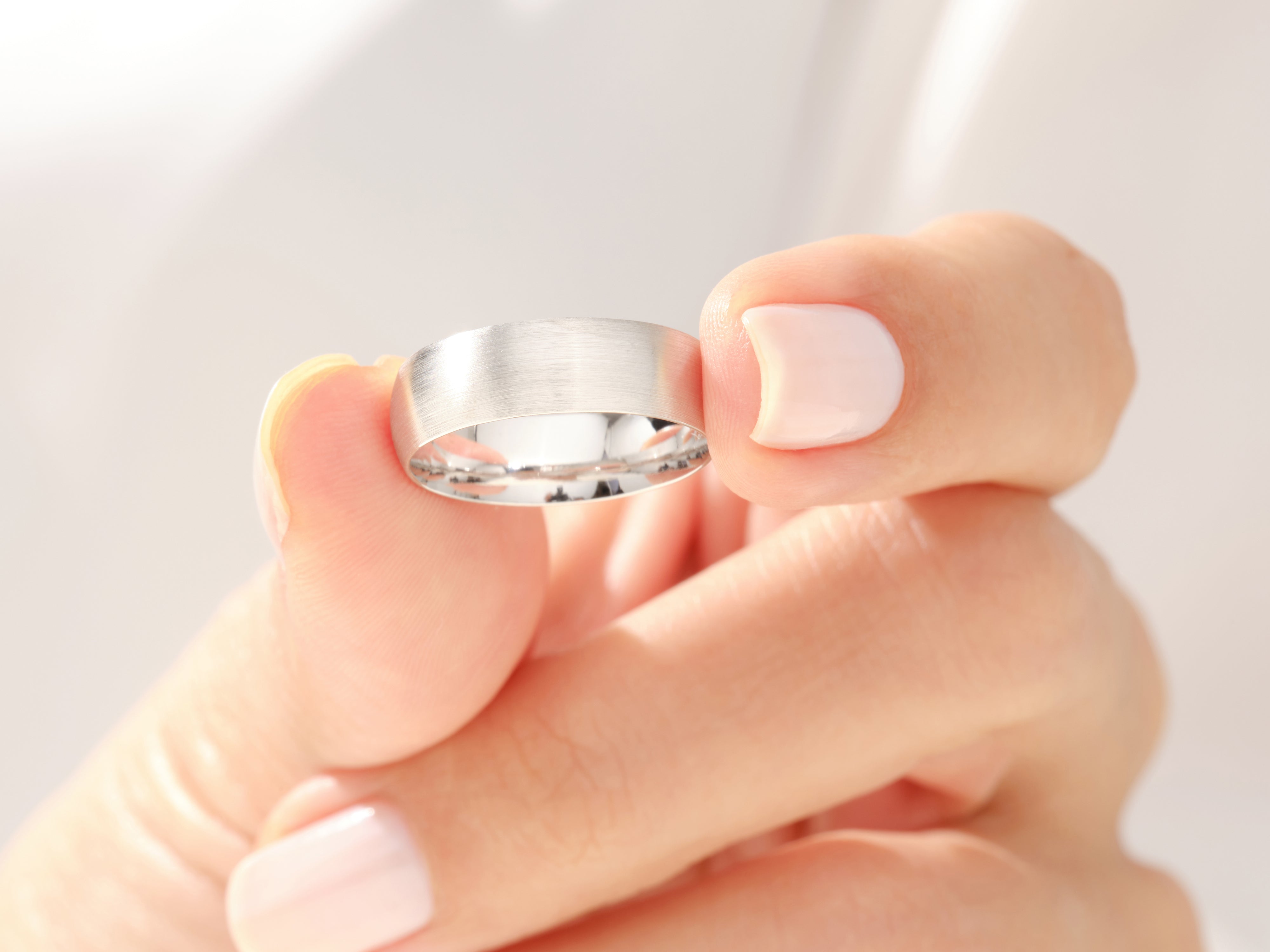 Brushed silver wedding band held by a manicured hand